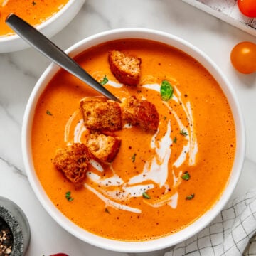 Roasted garlic tomato soup in a white bowl served with croutons with a white marble background.