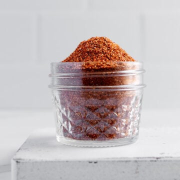 Homemade taco seasoning in a glass jar on a white cutting board with a white background.