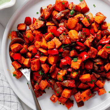 Sweet potato hash served on a white plate alongside a small bowl of cilantro lime sauce with a white background.
