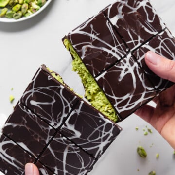 Hands breaking apart a homemade Dubai Chocolate Bar with a white marble background.