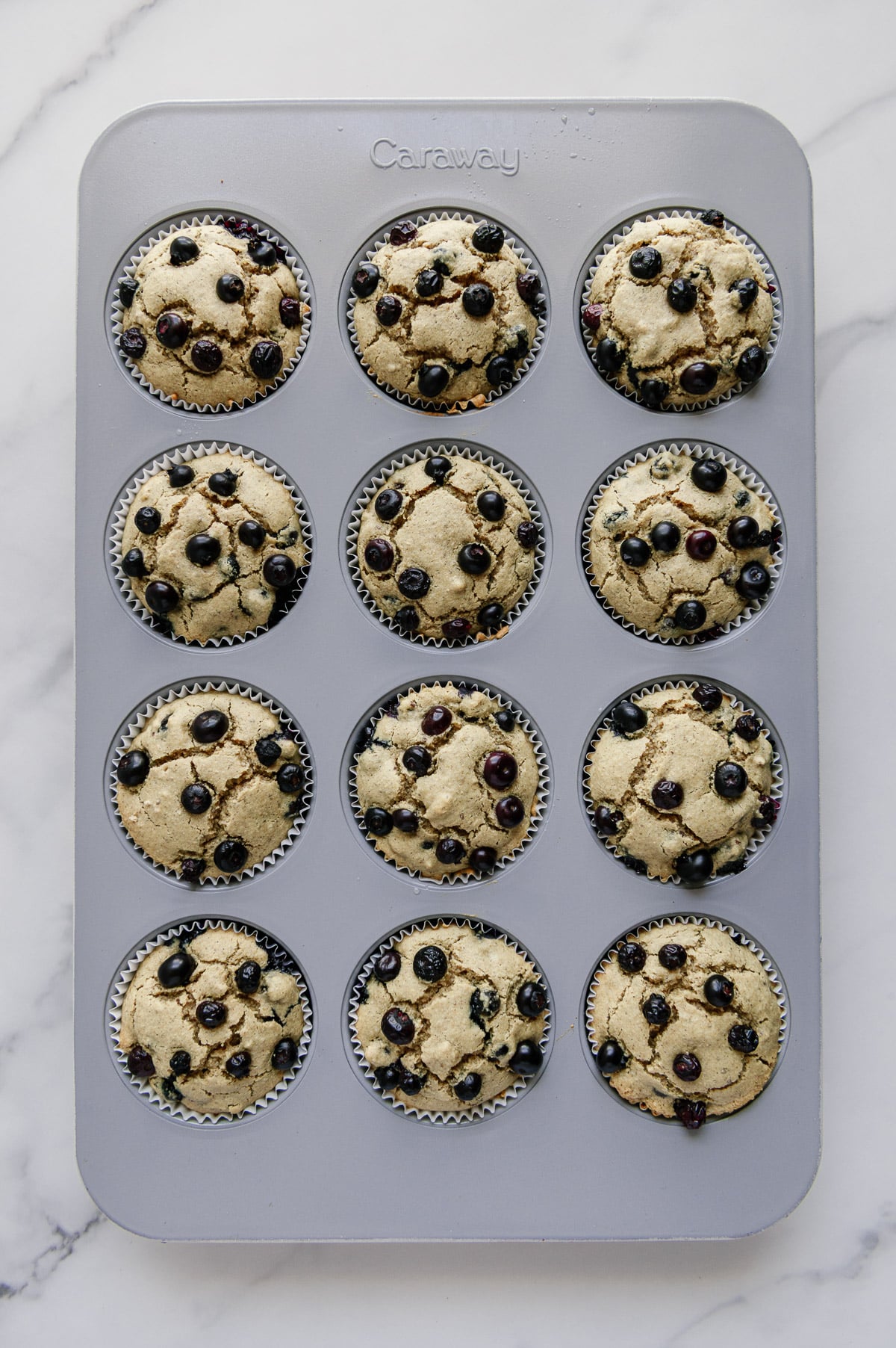 Baked blueberry muffins in a muffin tin with a white marble background.