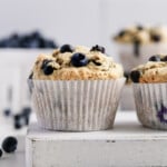 Vegan blueberry muffins on a white platter with fresh blueberries in the background.