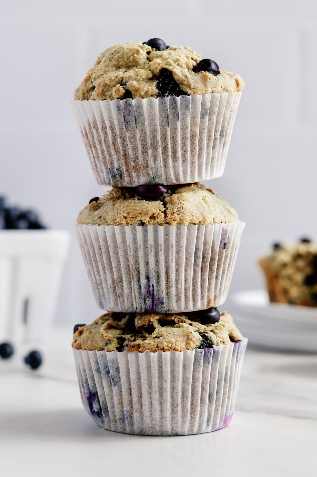Three vegan blueberry muffins stacked on top of each other with a white background.