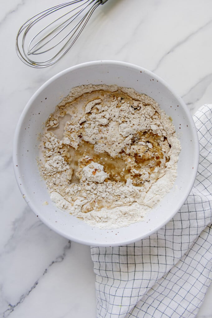 Wet ingredients added to dry ingredients in a white mixing bowl to make vegan blueberry muffins.