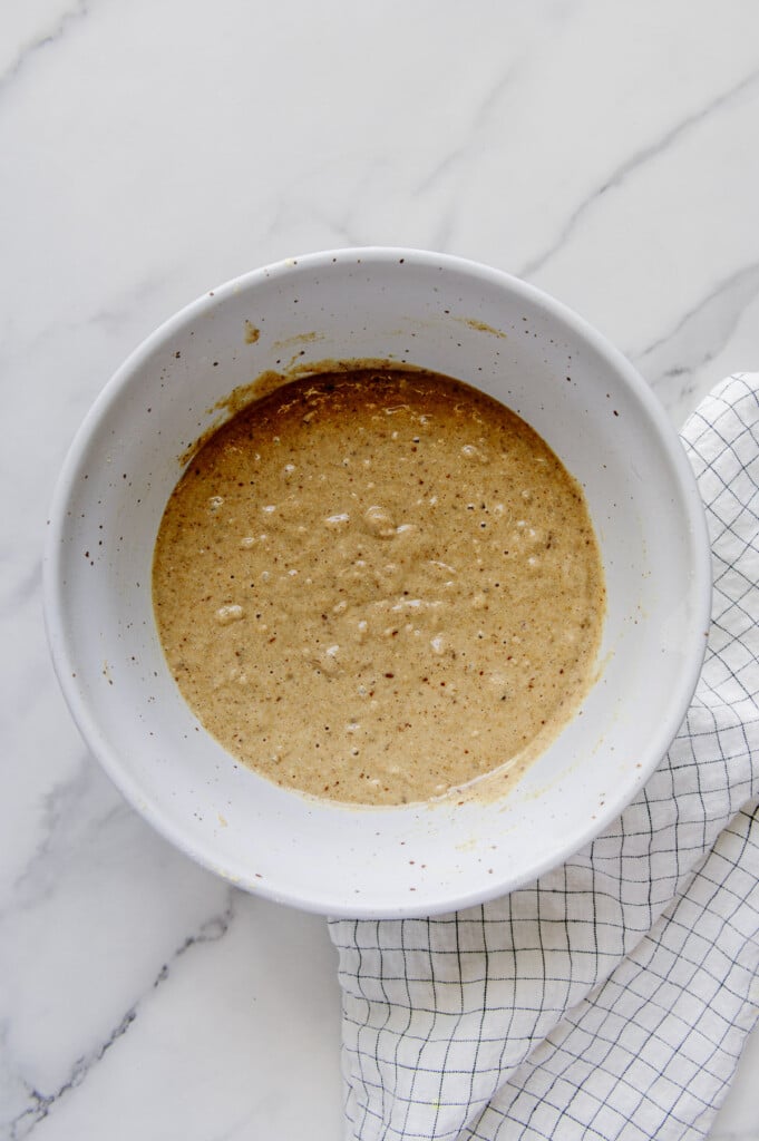 Mixture for vegan blueberry muffins in a white mixing bowl prior to baking.