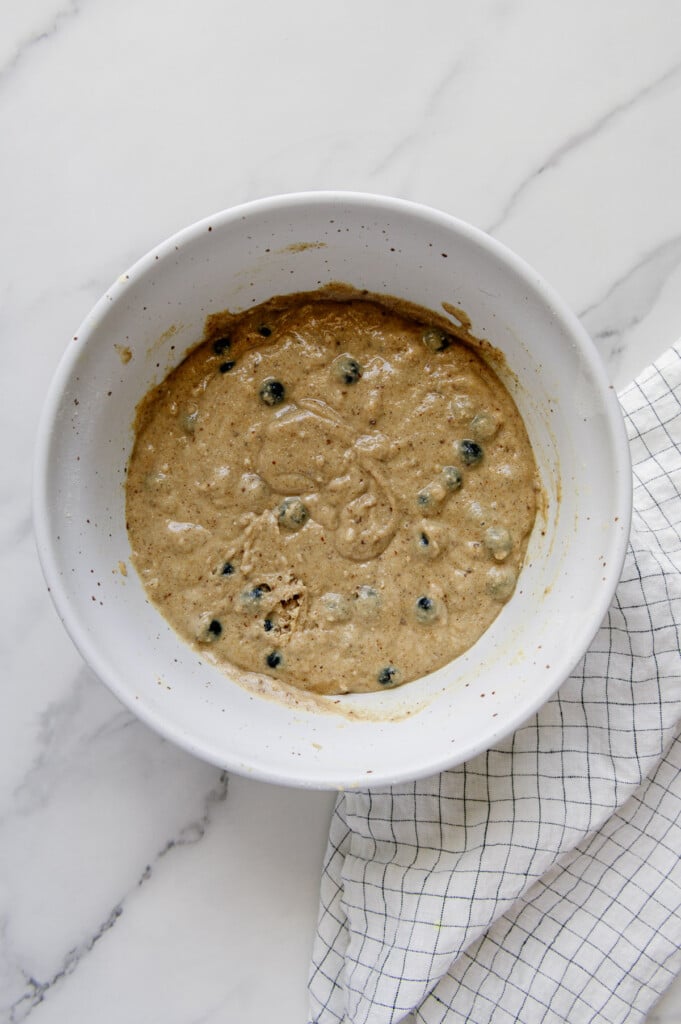 Mixture for vegan blueberry muffins in a white mixing bowl.