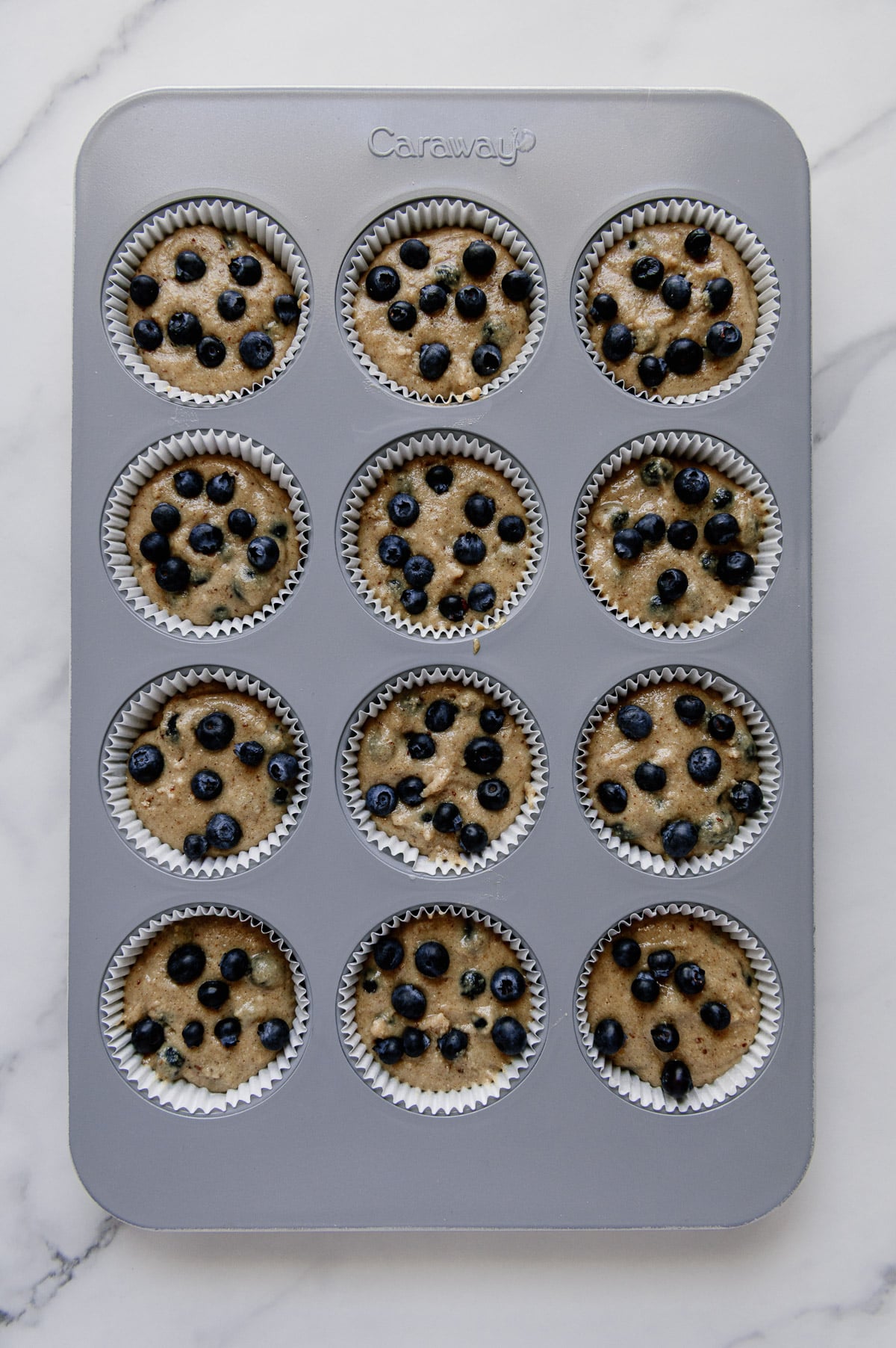 Vegan blueberry muffin mixture in a muffin tin to make 12 muffins.