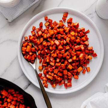 Roasted sweet potatoes served on a white circular plate with a white marble background.