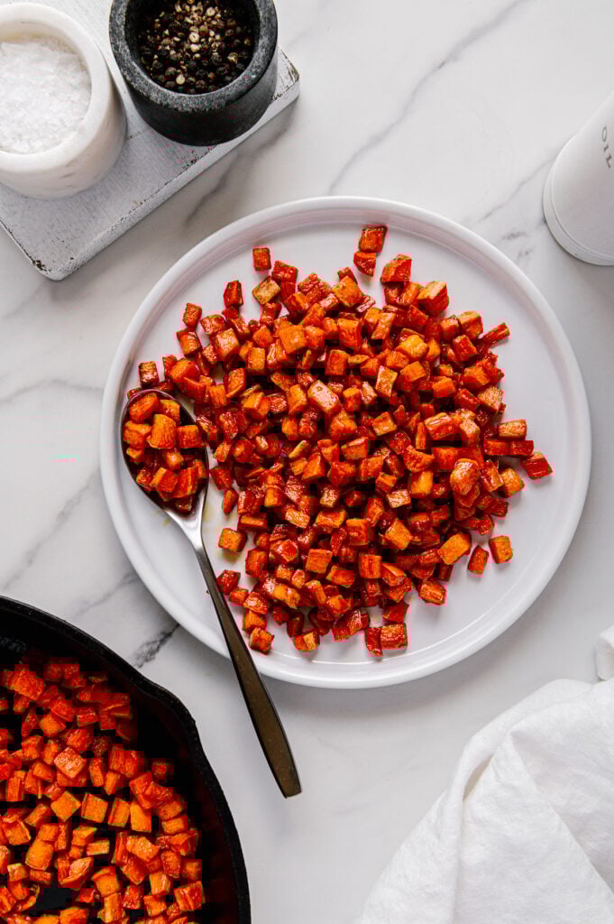 Roasted sweet potatoes served on a white circular plate with a white marble background.