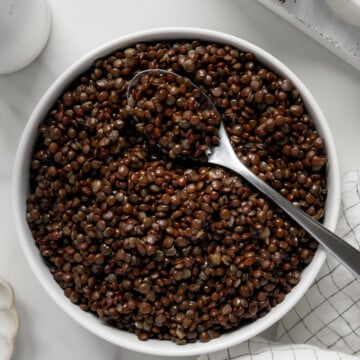 Black lentils in a white bowl served with a silver spoon with a white background.