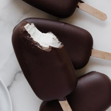 Vegan ice cream bars on popsicle sticks with a white marble background.