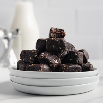 Chocolate tahini bites on a stack of white plates with a white background.