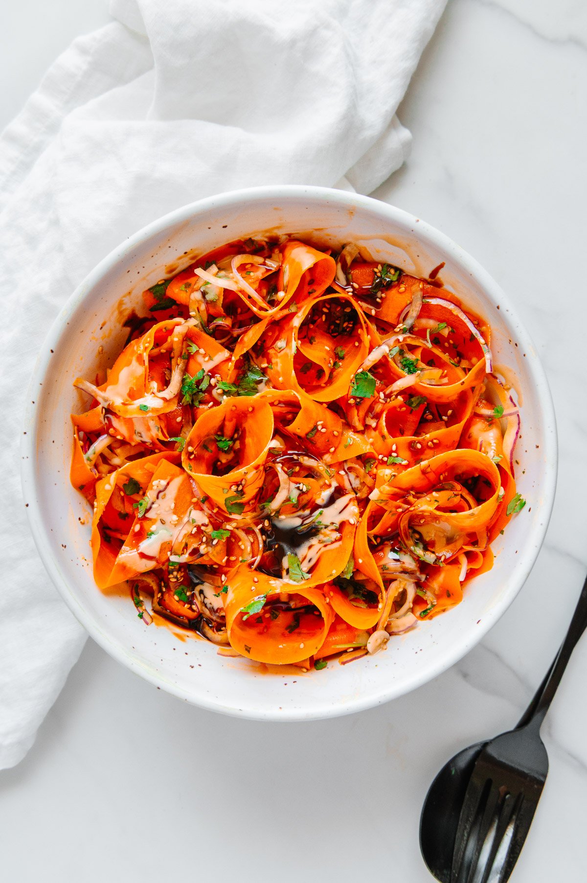 Carrot ribbon salad in a white bowl with a white marble background.