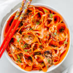 Carrot ribbon salad in a white bowl served with red chopsticks with a white background.