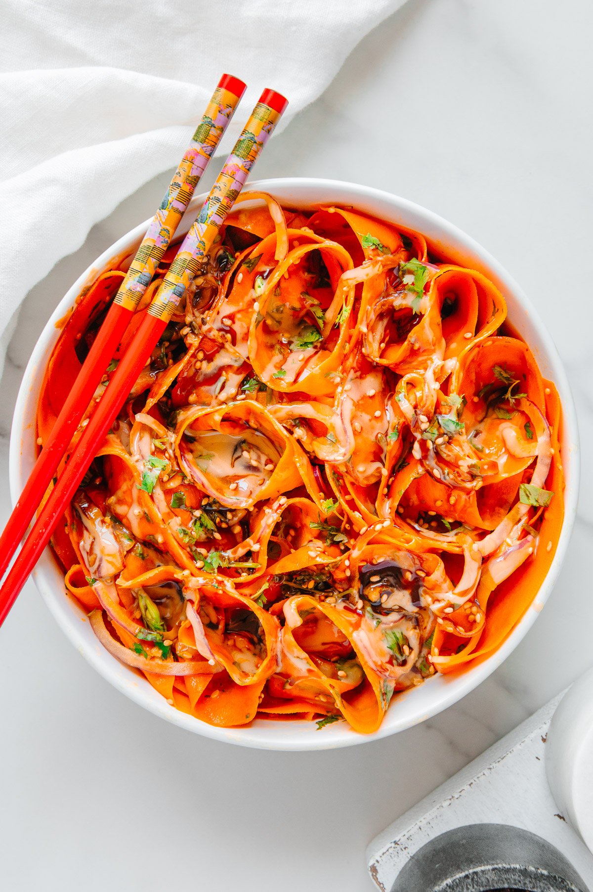 Carrot ribbon salad in a white bowl served with red chopsticks with a white background.