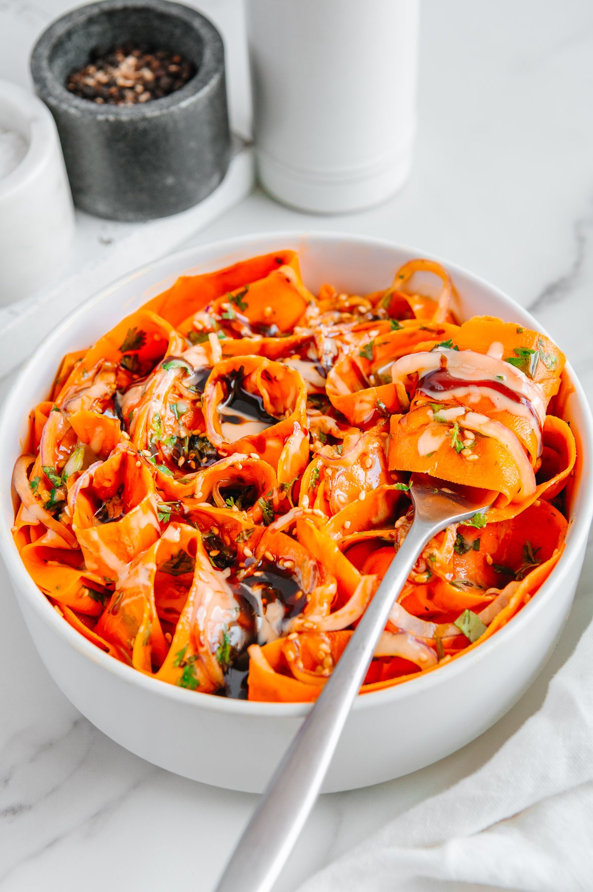 Carrot ribbon salad in a white bowl served with a silver fork with a carrot ribbon wrapped around it.