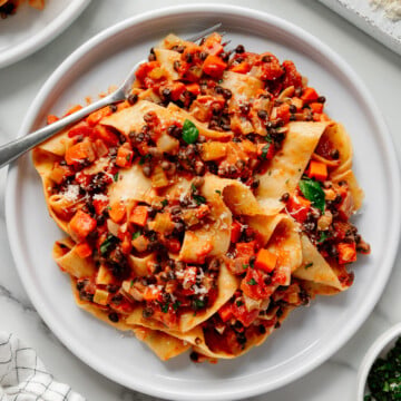Lentil bolognese on a white plate with a silver fork with a white marble background.