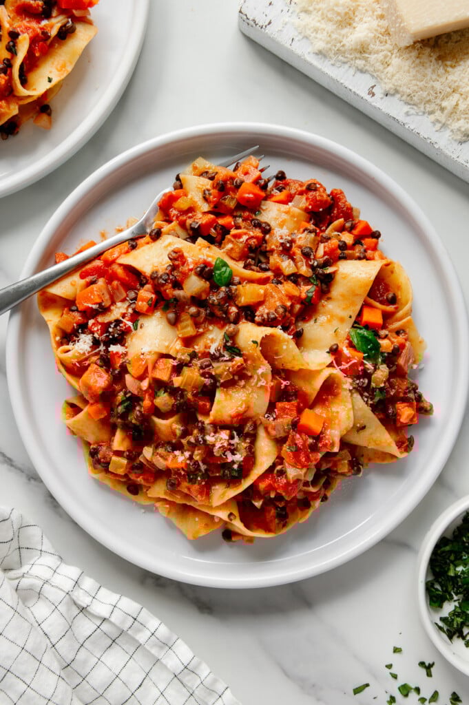 Lentil bolognese on a white plate with a silver fork with a white marble background.