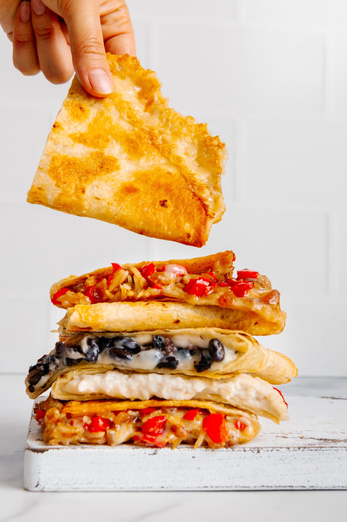 A stack of vegan quesadillas with various fillings in each with a white background.