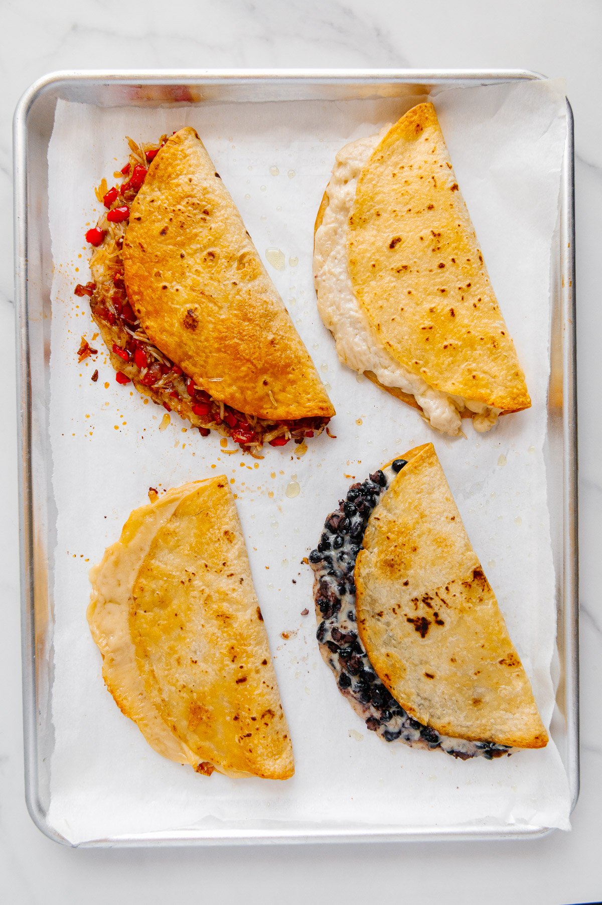 Four various vegan quesadillas after being baked on a sheetpan lined with parchment paper.