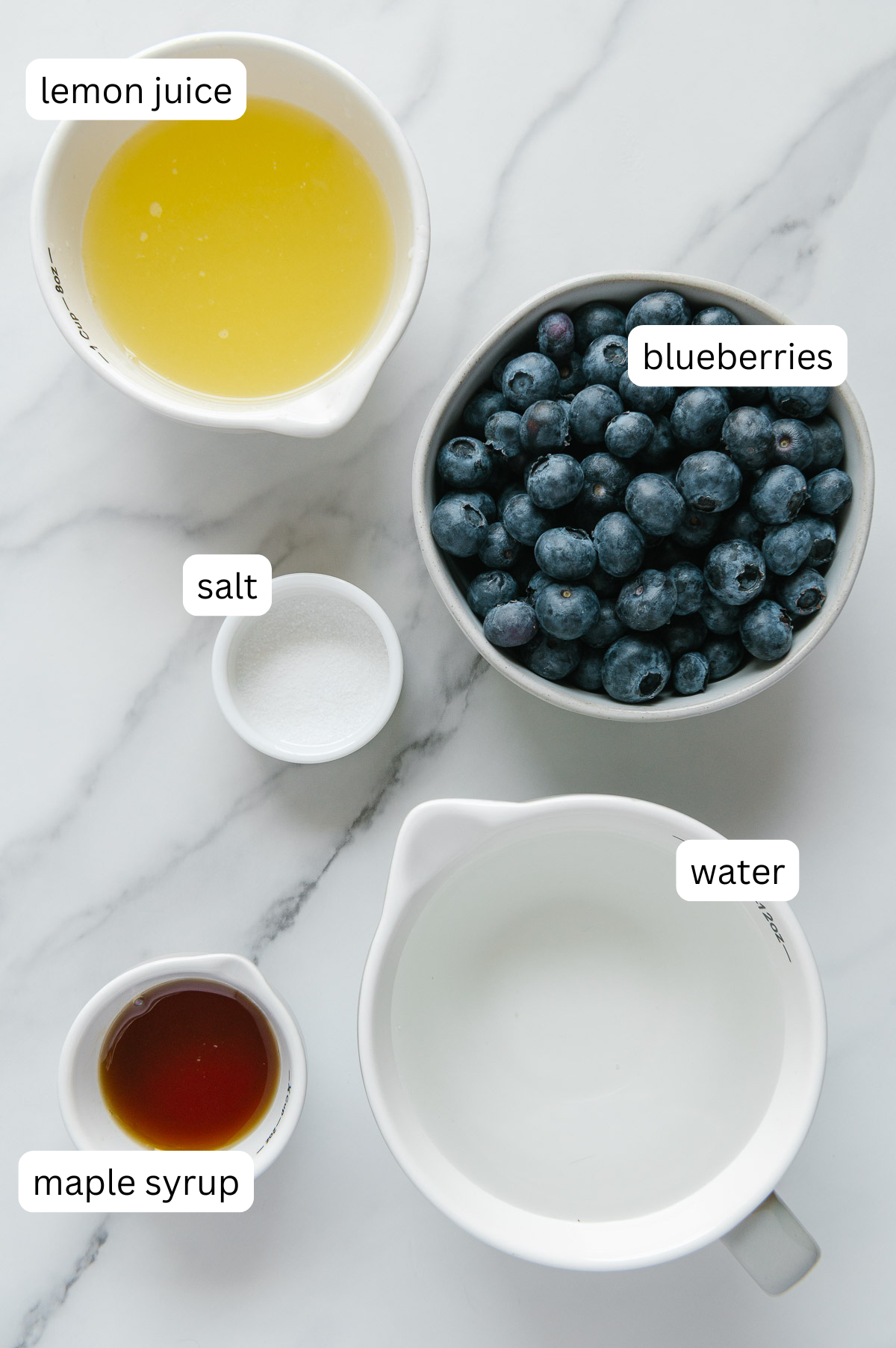 Ingredients of fresh blueberry lemonade with a white marble background.