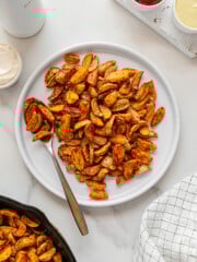 Crispy roasted potatoes served on a white plate with a white marble background.