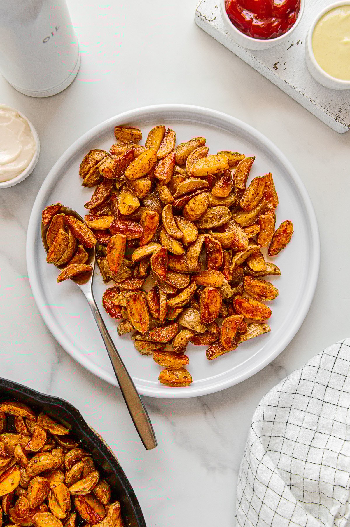 Crispy roasted potatoes served on a white plate with a white marble background.
