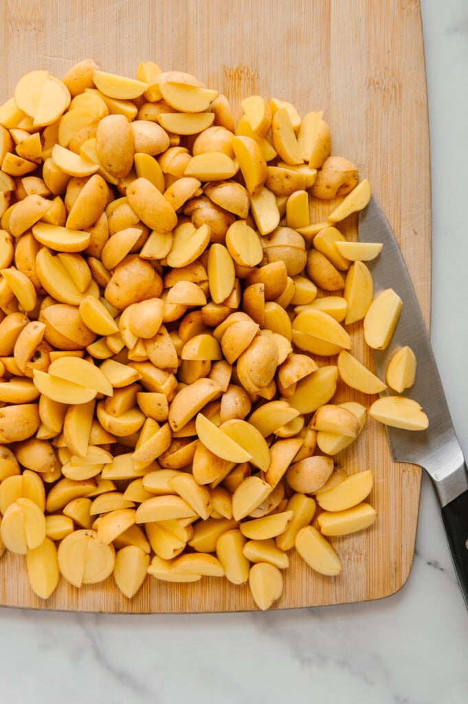 Baby Dutch Yellow potatoes cut into quarters on a wooden cutting board.