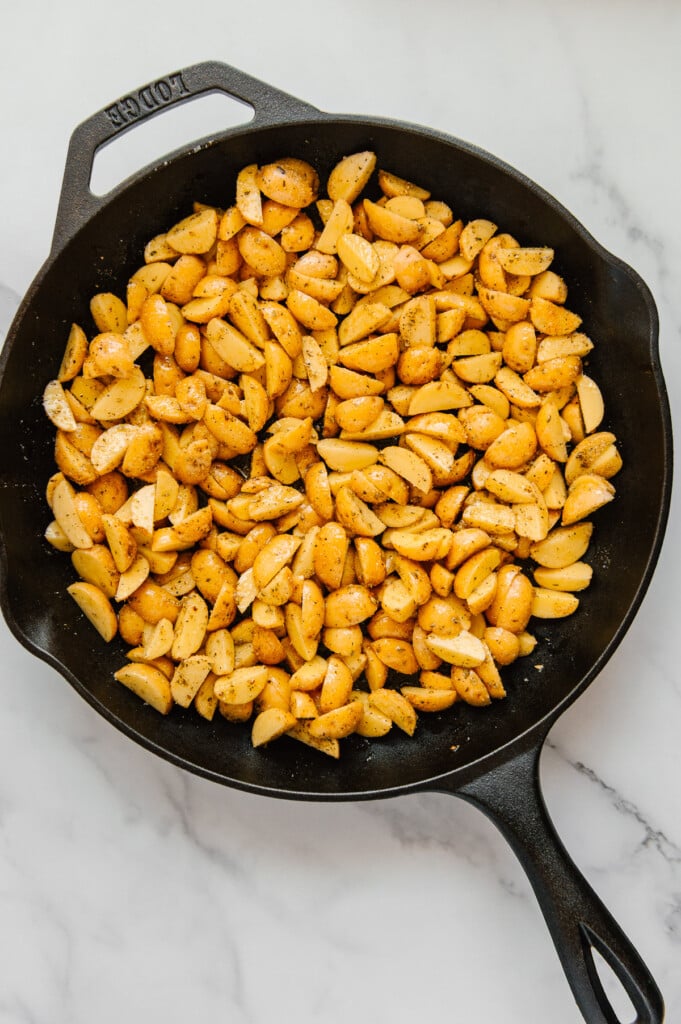 Quartered Baby Dutch Yellow potatoes in a cast iron skillet with a white marble background.