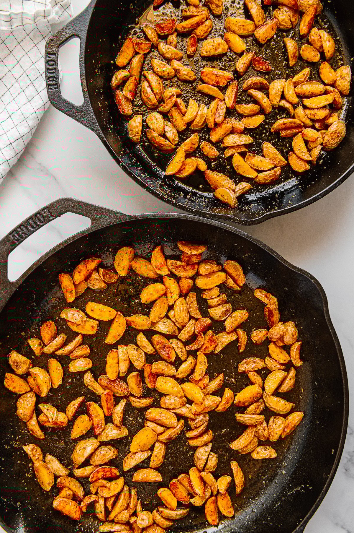 Roasted Baby Dutch Yellow potatoes in two cast iron skillets with a white marble background.
