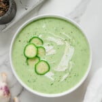 Cold Cucumber Soup in a white bowl - overhead shot with white background and garnished with cucumber slices and cream