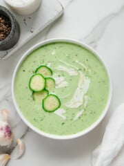 Cold Cucumber Soup in a white bowl - overhead shot with white background and garnished with cucumber slices and cream