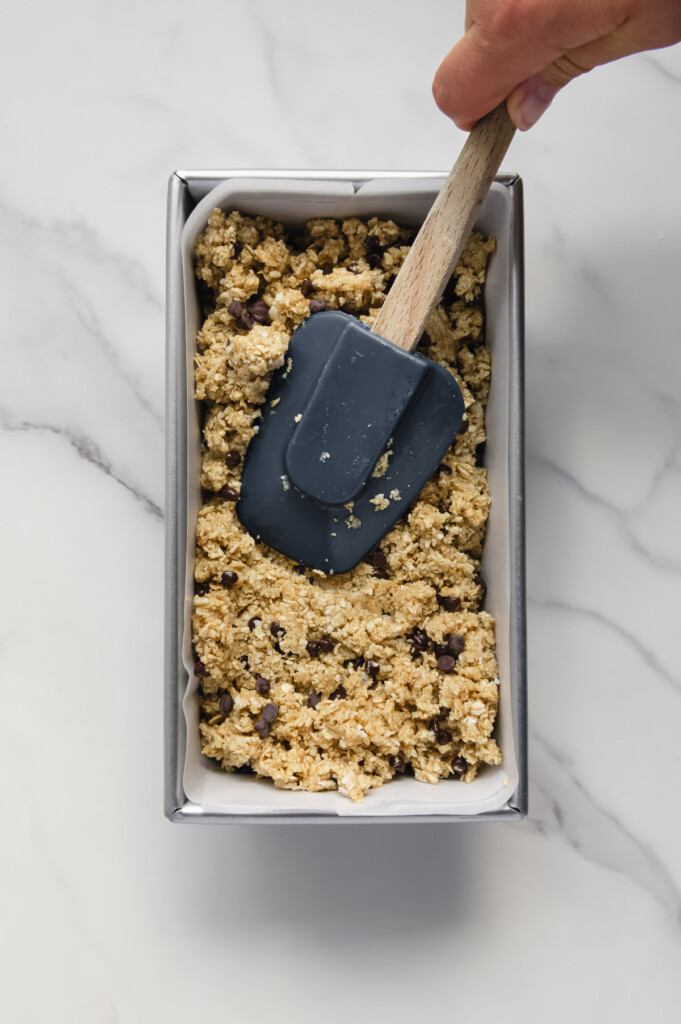 Using a spatula to pack the Heavenly Hunks mixture into a loaf pan.