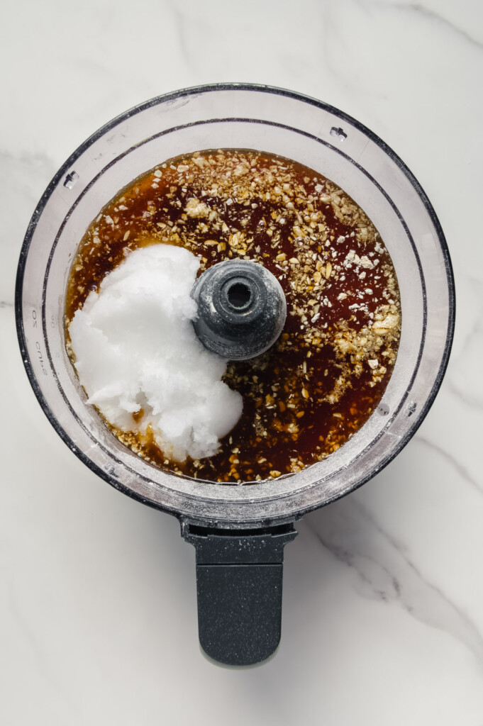 Maple syrup and coconut oil added to dry ingredients in a food processor.