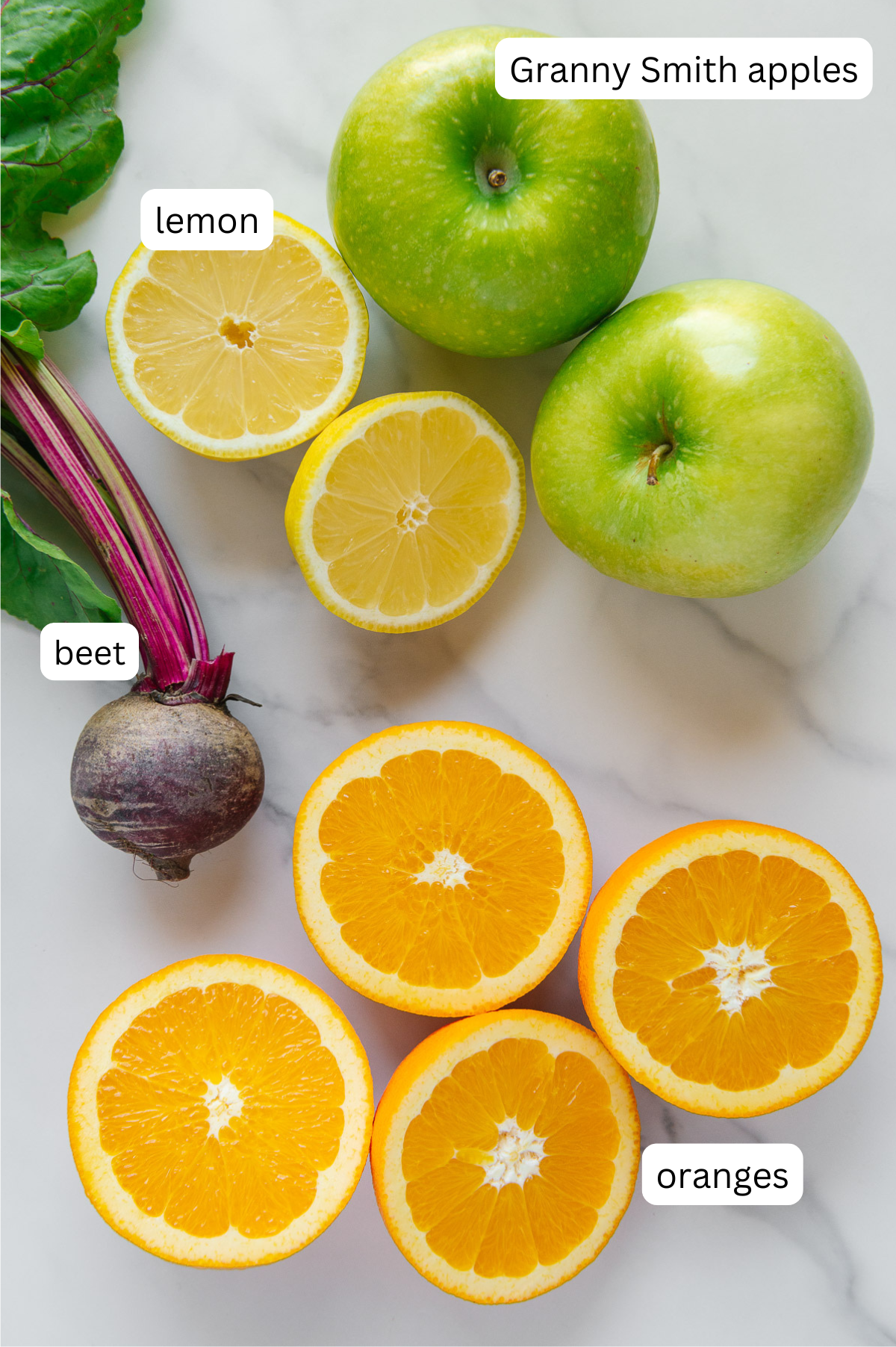 Apples, lemon, beet and oranges with a white marble background.