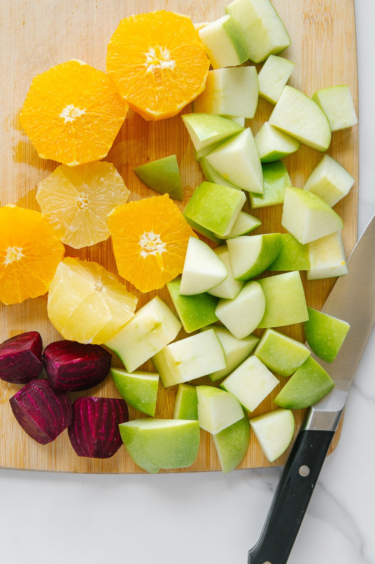 Sliced orange, apples, beet and lemon on a wooden cutting board with a sharp knife.
