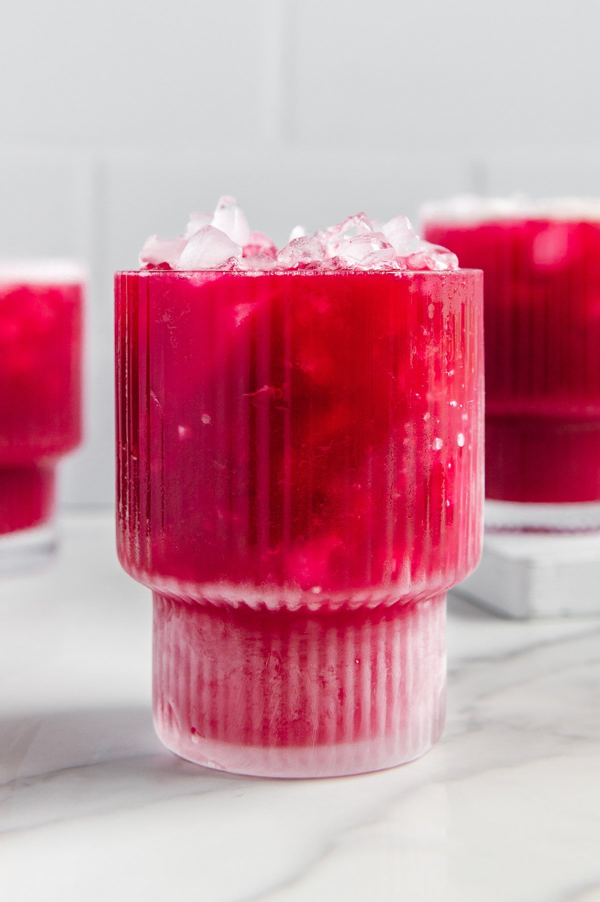 Three glasses of fruit punch with a white marble background.