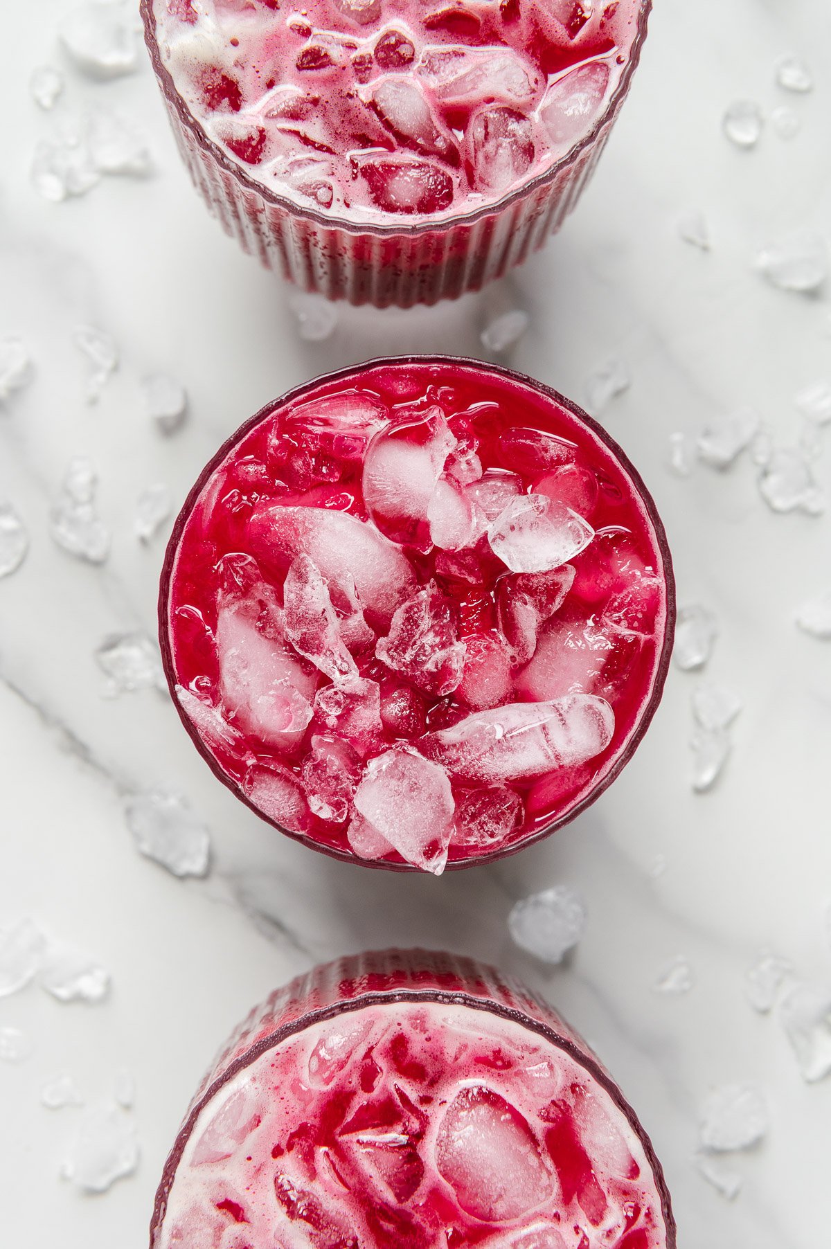 Overhead angle of three glasses of nature's fruit punch filled with ice with a white marble background.