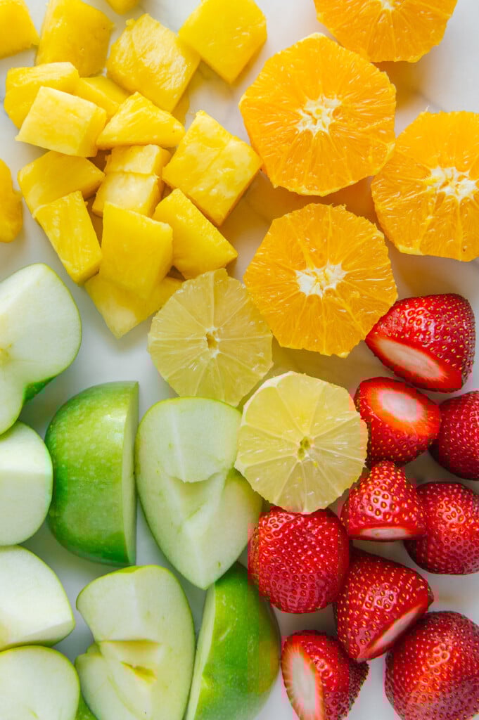 Sliced pineapple, orange, lemon, apple and strawberries with a white background.