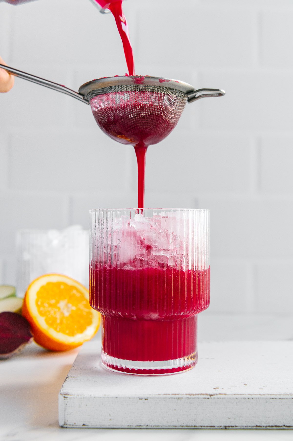 Pouring Nature's Fruit Punch through a strainer into a glass filled with ice with a white background.