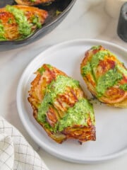 Two roasted cabbage wedges served on a white plate with a lemon herb tahini sauce drizzled overtop.