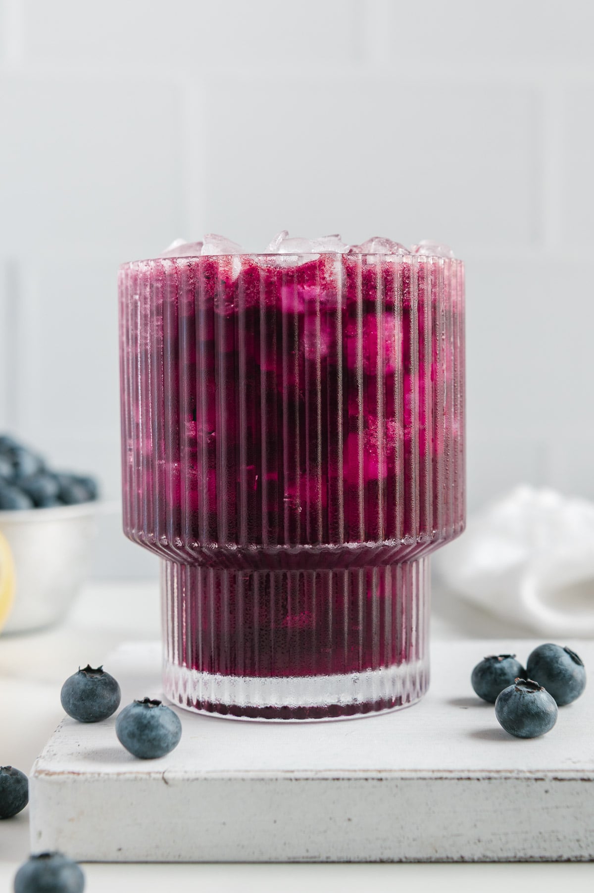 Blueberry lemonade in a glass next to fresh blueberries with a white background.