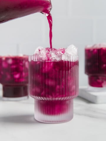 Fresh blueberry lemonade being poured in a glass filled with crushed ice on a white background