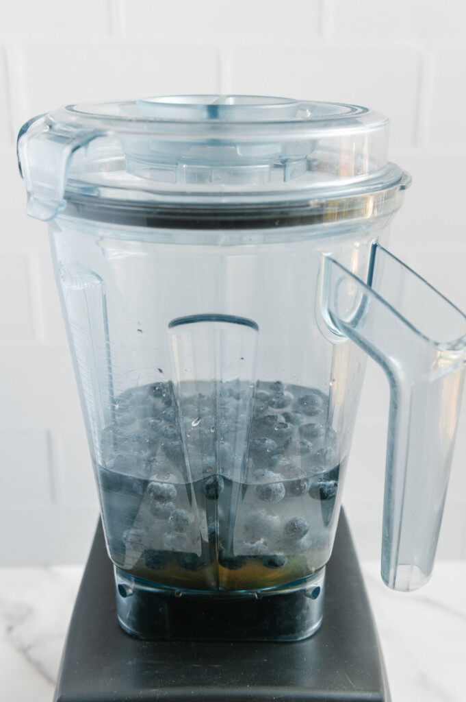 Blueberries, lemon juice, water, salt and maple syrup in a blender prior to blending with a white background.