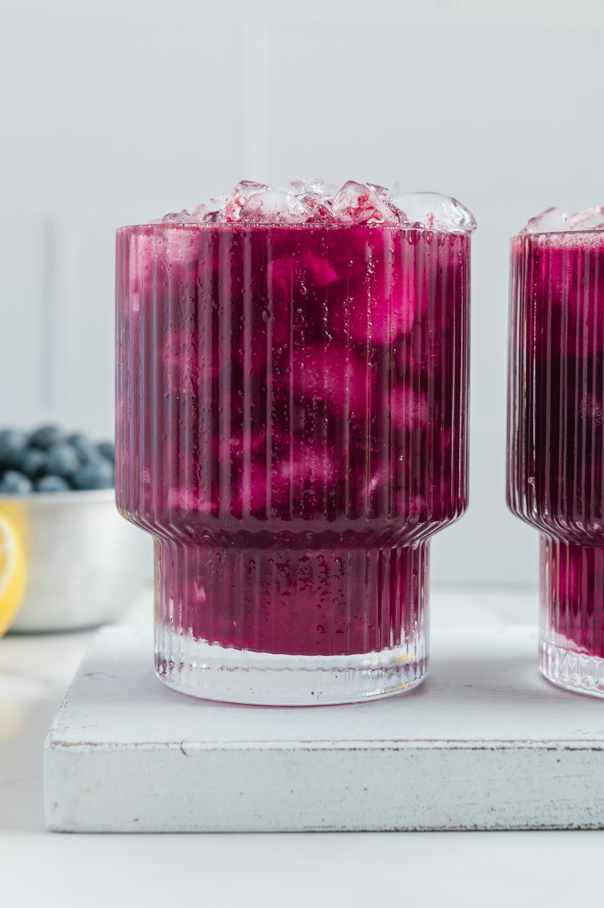 Fresh blueberry lemonade in two glasses filled with ice with a white background.