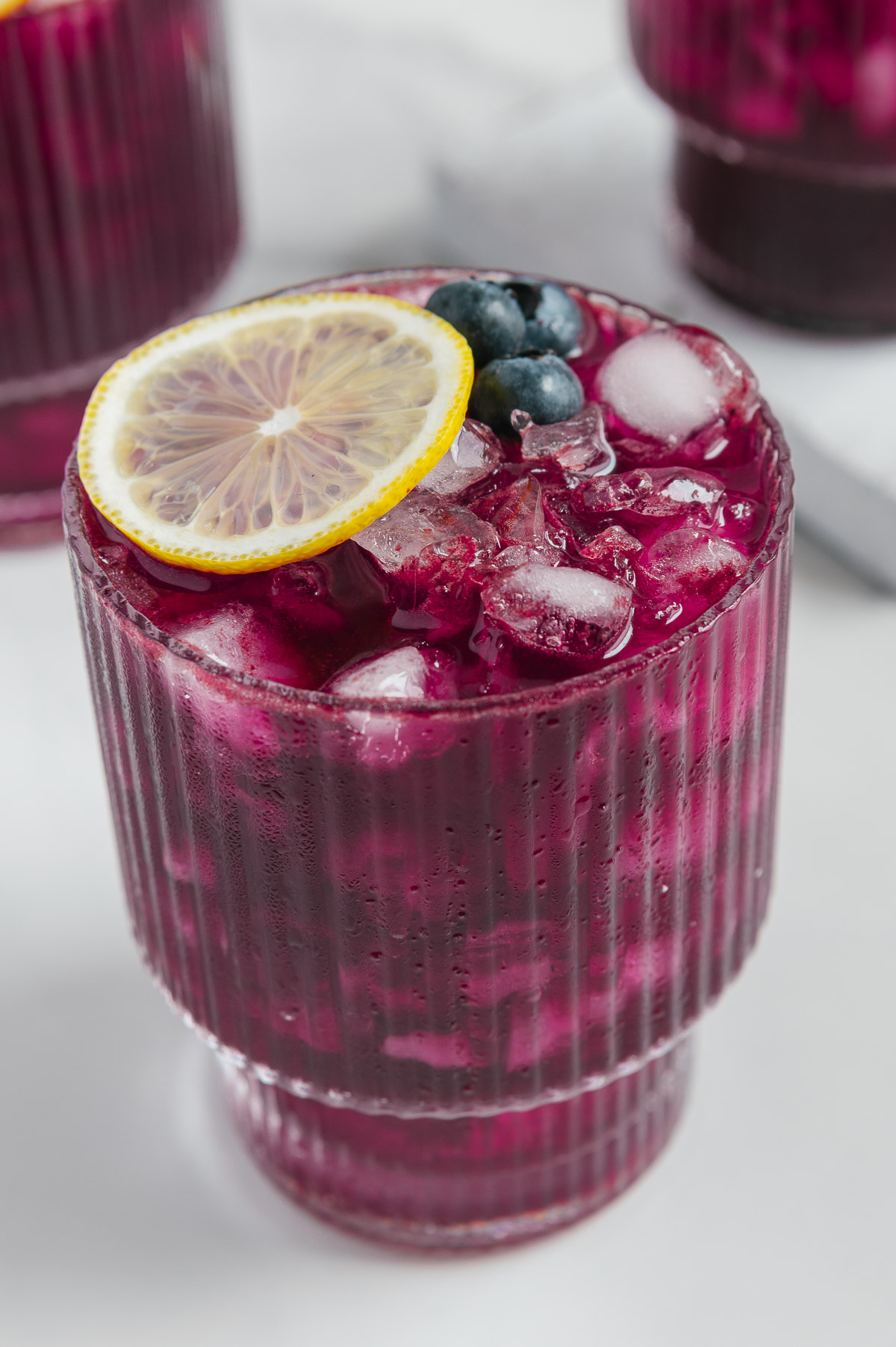 Blueberry lemonade in a glass filled with ice and garnished with a lemon slice and fresh blueberries.