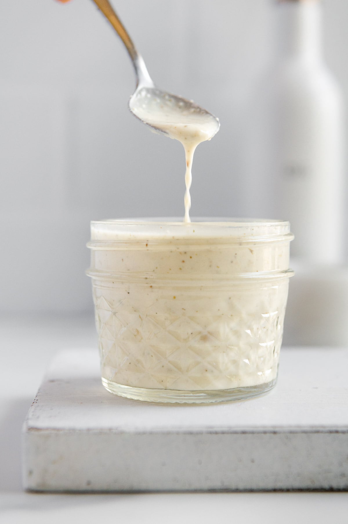 Vegan Italian dressing dripping from a spoon into a small glass jar of homemade Italian dressing with a white background.
