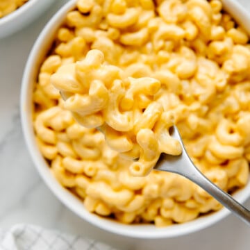 A bite of vegan mac and cheese on a fork over a white bowl of vegan mac and cheese.