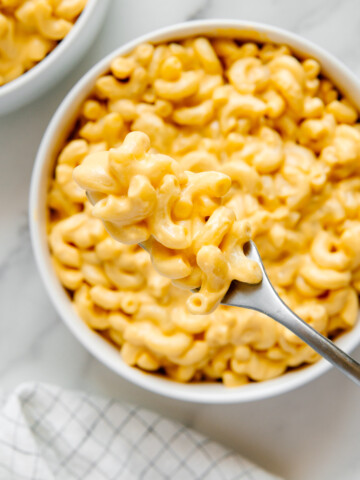 A bite of vegan mac and cheese on a fork over a white bowl of vegan mac and cheese.