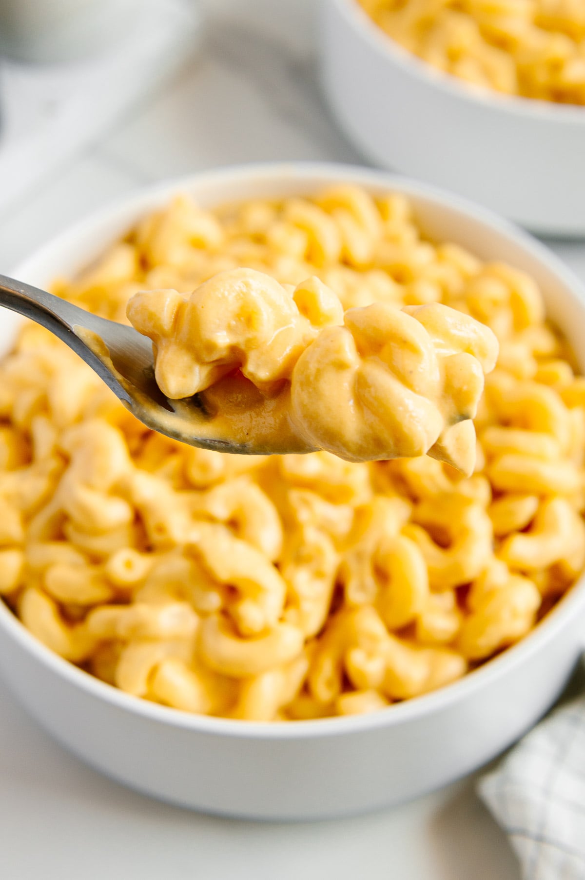 A close up of a bite of vegan mac and cheese on a fork held over a bowl of vegan mac and cheese.